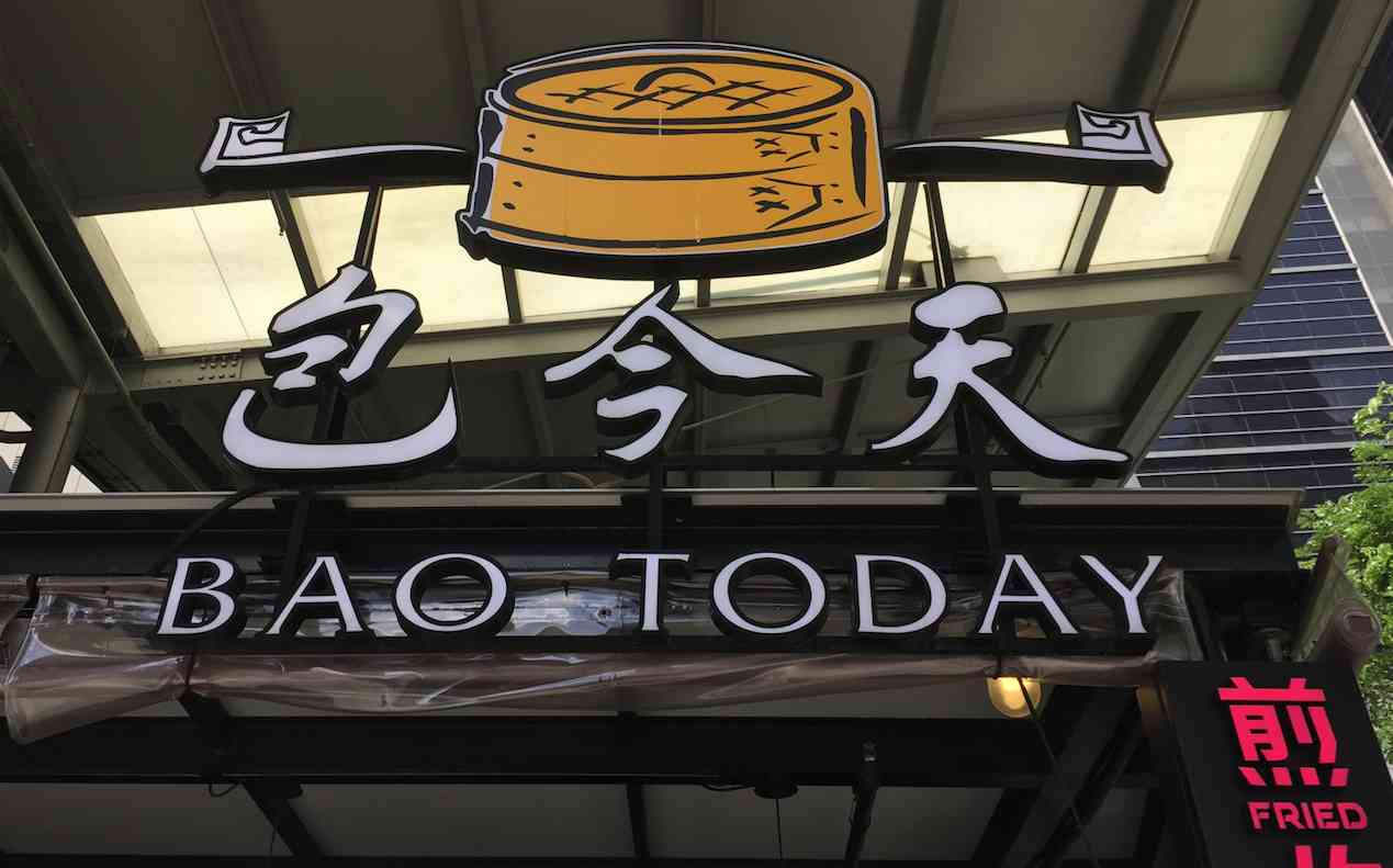 Sign for "bao today" restaurant featuring cartoon images of a steaming bun and a man with a bowl under an awning.