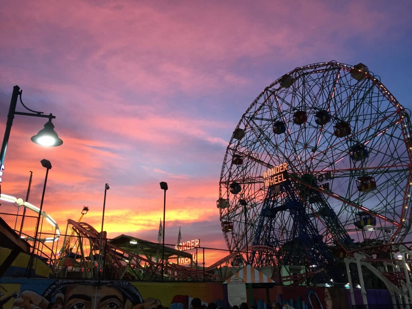 A vibrant sunset sky behind the wonder wheel and amusement park rides at coney island.