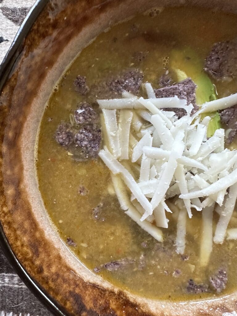 A bowl of soup with cheese and avocado.