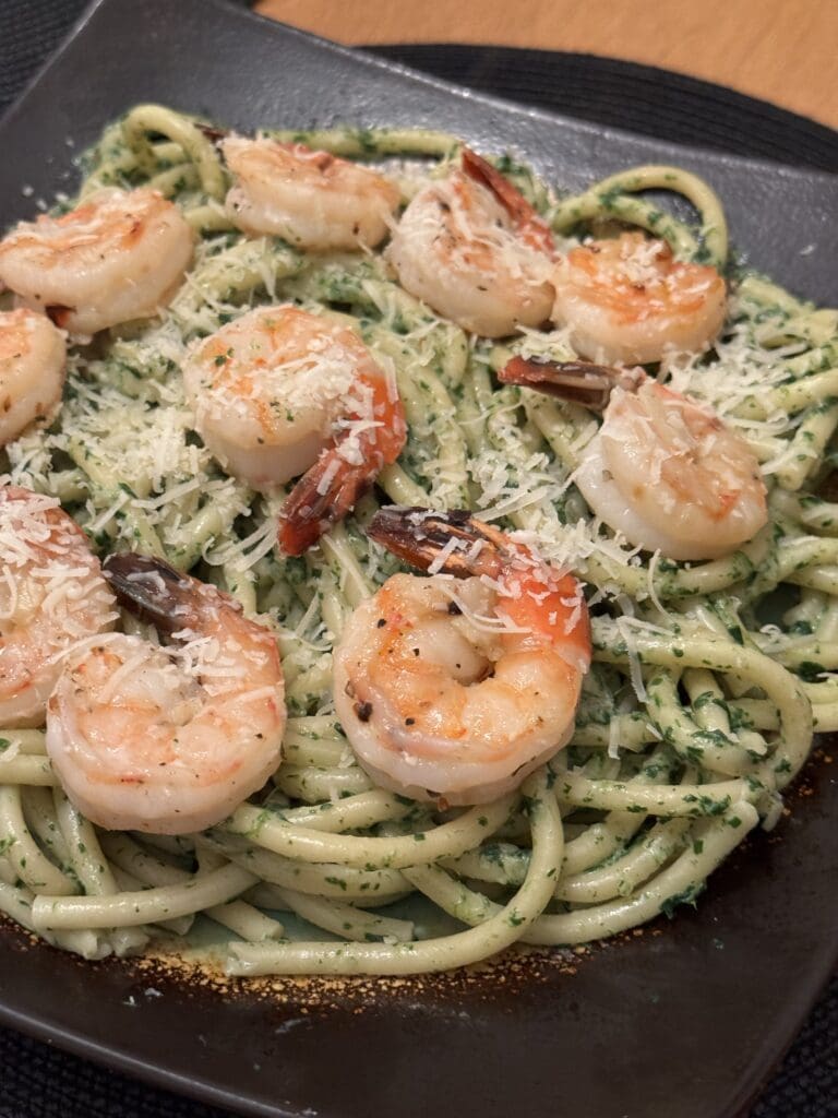 A plate of linguine pasta with pesto sauce topped with grilled shrimp and sprinkled with grated parmesan cheese.
