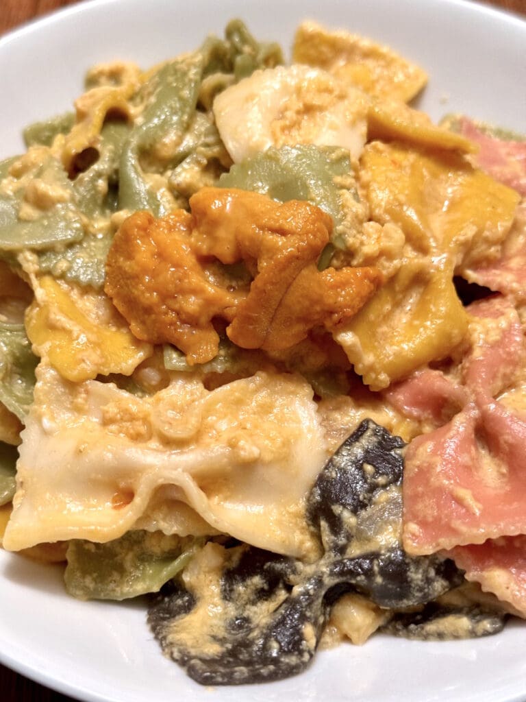 A close-up of a colorful pasta dish with various shades and textures, served on a white plate.