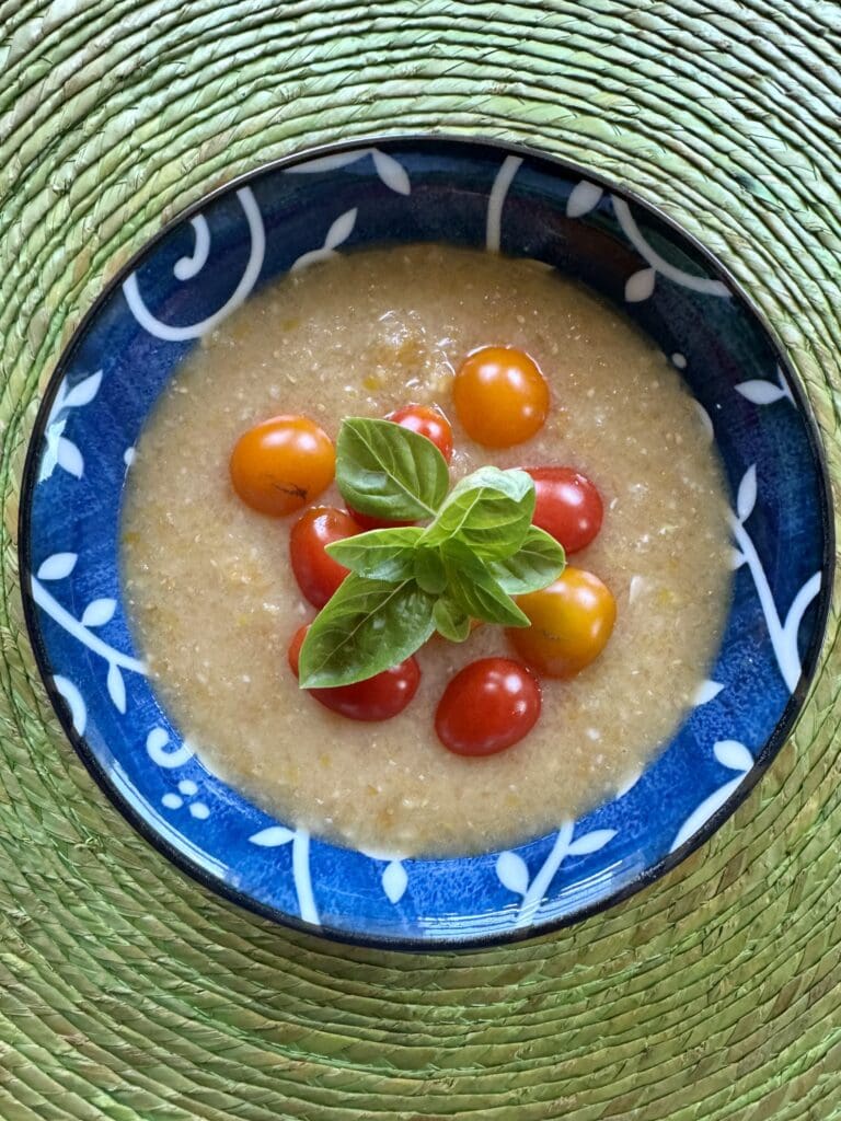 Creamy soup with tomatoes and basil in a blue bowl.