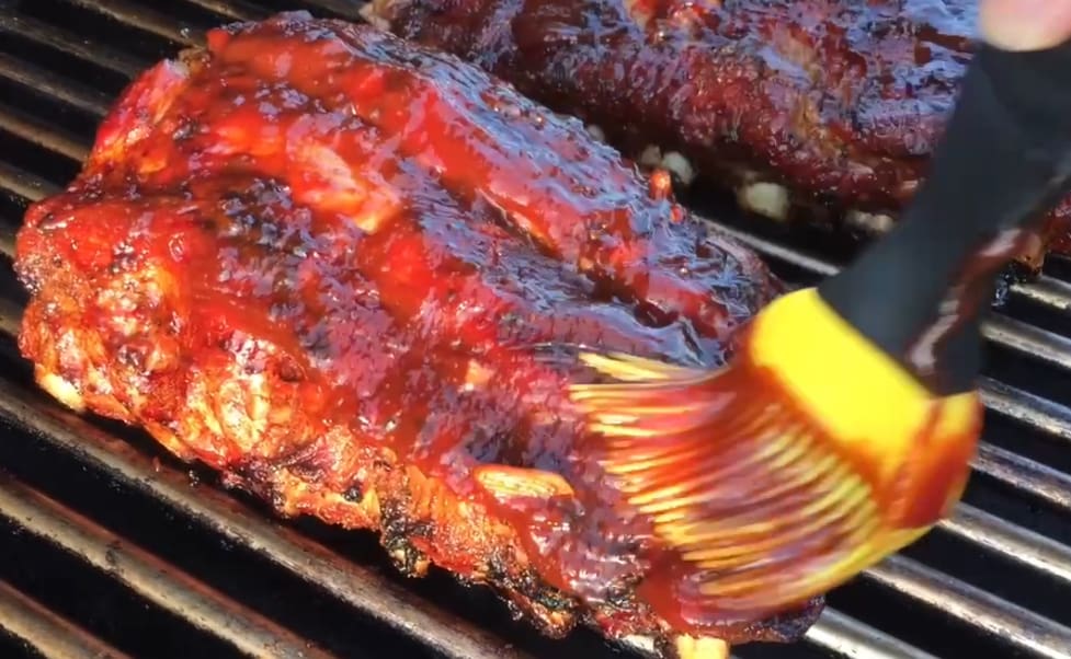 BBQ ribs being basted on a grill.