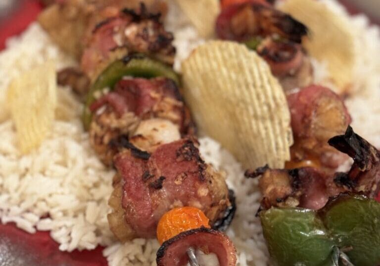 Bacon skewers with rice and peppers on a plate.