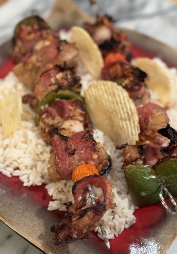 Bacon skewers with rice and peppers on a plate.