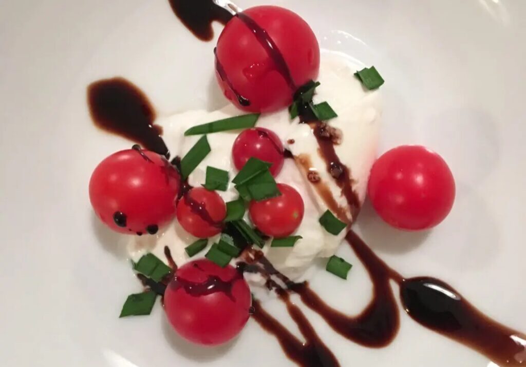 Caprese salad with balsamic reduction on a white plate, featuring fresh mozzarella, cherry tomatoes, and basil.