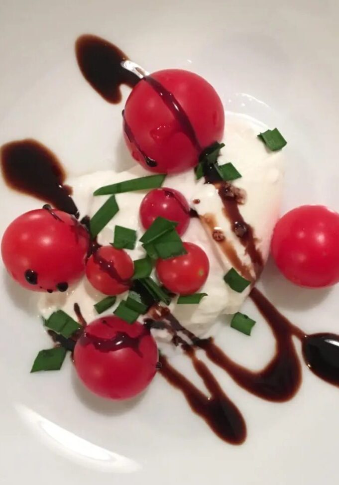 Caprese salad with balsamic reduction on a white plate, featuring fresh mozzarella, cherry tomatoes, and basil.
