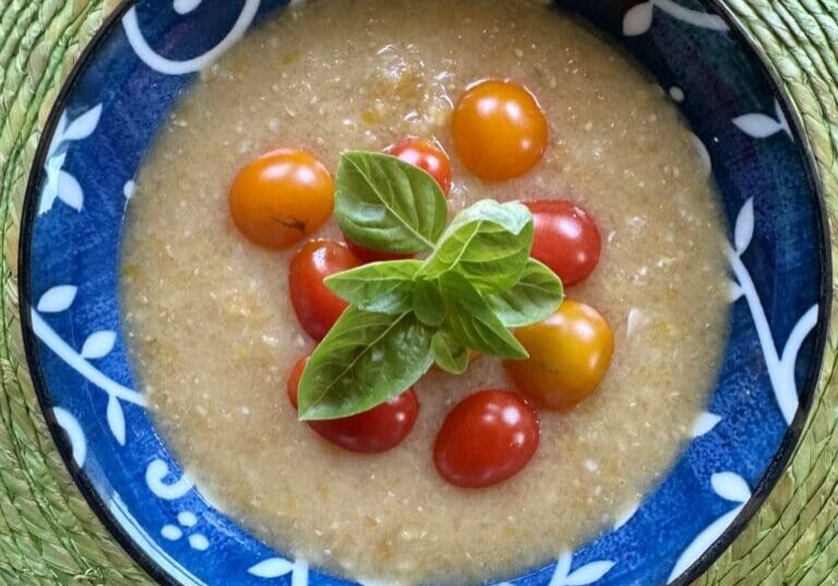 Creamy soup with tomatoes and basil in a blue bowl.