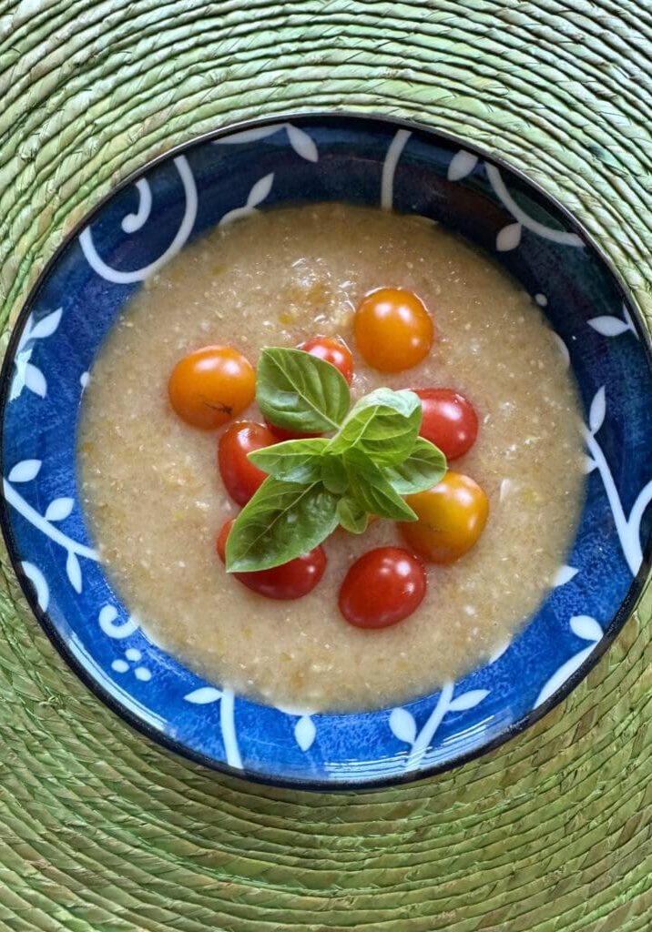 Creamy soup with tomatoes and basil in a blue bowl.