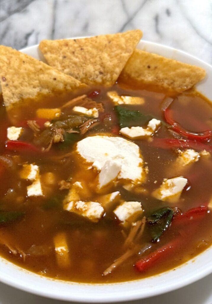 Bowl of soup with tortillas and toppings.