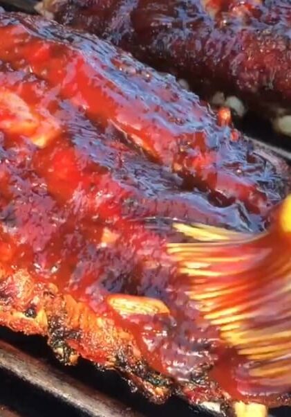 BBQ ribs being basted on a grill.