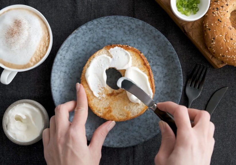 Spreading cream cheese on bagel. Healthy tasty breakfast food. Top view