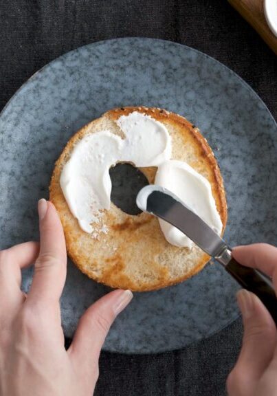 Spreading cream cheese on bagel. Healthy tasty breakfast food. Top view