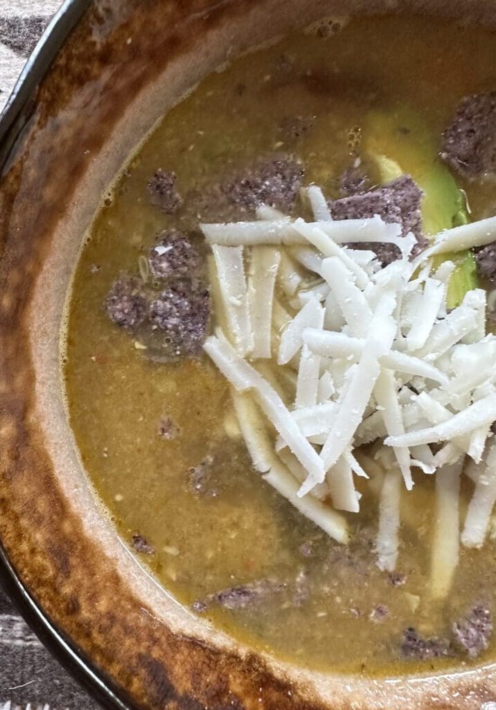A bowl of soup with cheese and avocado.